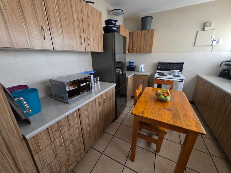 Functional kitchen featuring wood-look laminate cabinetry, tiled flooring, a tiled backsplash, and a freestanding stove with ample counter space.