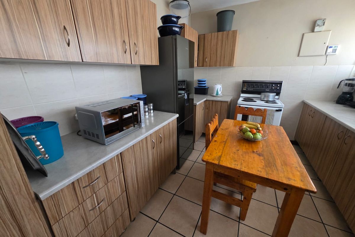 Functional kitchen featuring wood-look laminate cabinetry, tiled flooring, a tiled backsplash, and a freestanding stove with ample counter space.