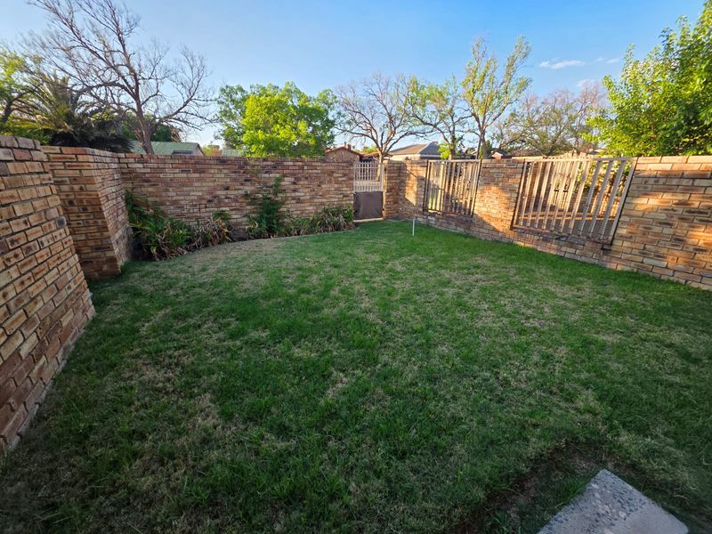 A private rear garden featuring a lawn area enclosed by brick boundary walls and timber slat fencing with a rear access gate.