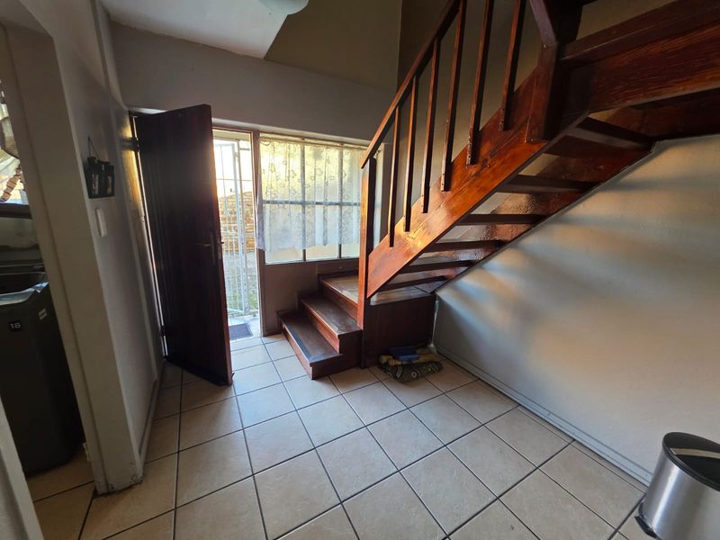 Entrance area featuring tiled flooring and a wooden staircase leading to the upper level, with direct access to the exterior through a timber door.