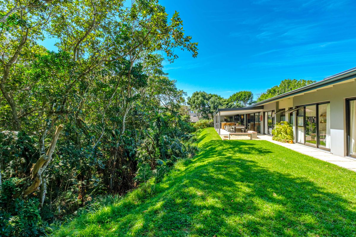 A well-maintained rear exterior view featuring a lush green lawn, a covered patio area, and large sliding glass doors opening to the garden.
