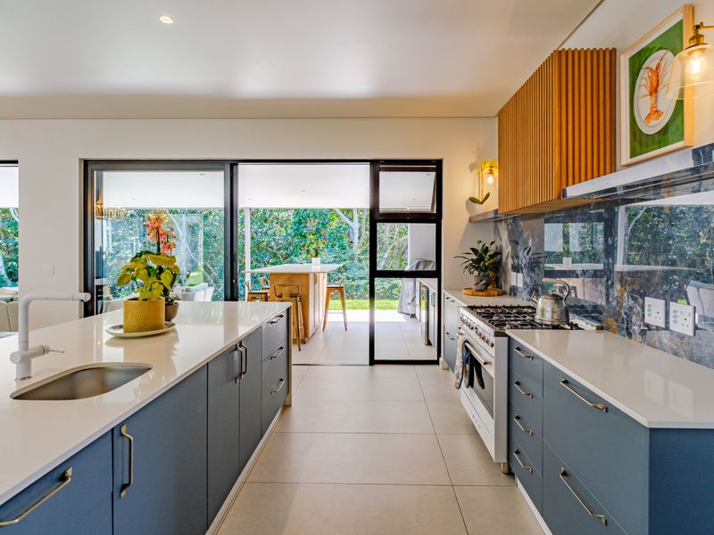 Modern kitchen featuring a central island, stone countertops, gas cooktop, and stylish slatted timber cabinetry, with seamless flow to an outdoor patio area.
