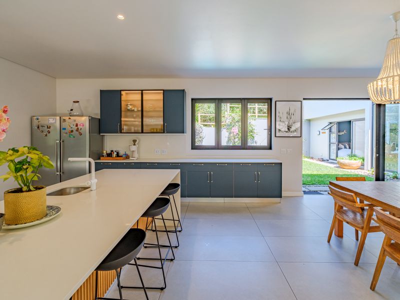 Modern open-plan kitchen featuring a central island, sleek cabinetry, and seamless flow to the outdoor patio area through large sliding glass doors.