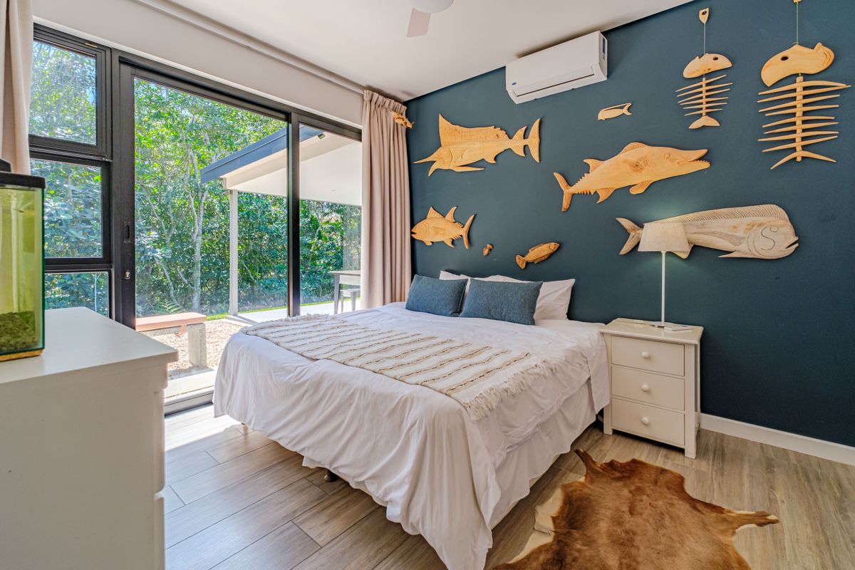 A bright bedroom featuring wood-look tile flooring, a split-system air conditioner, and large sliding glass doors providing direct access to the outdoor patio area.