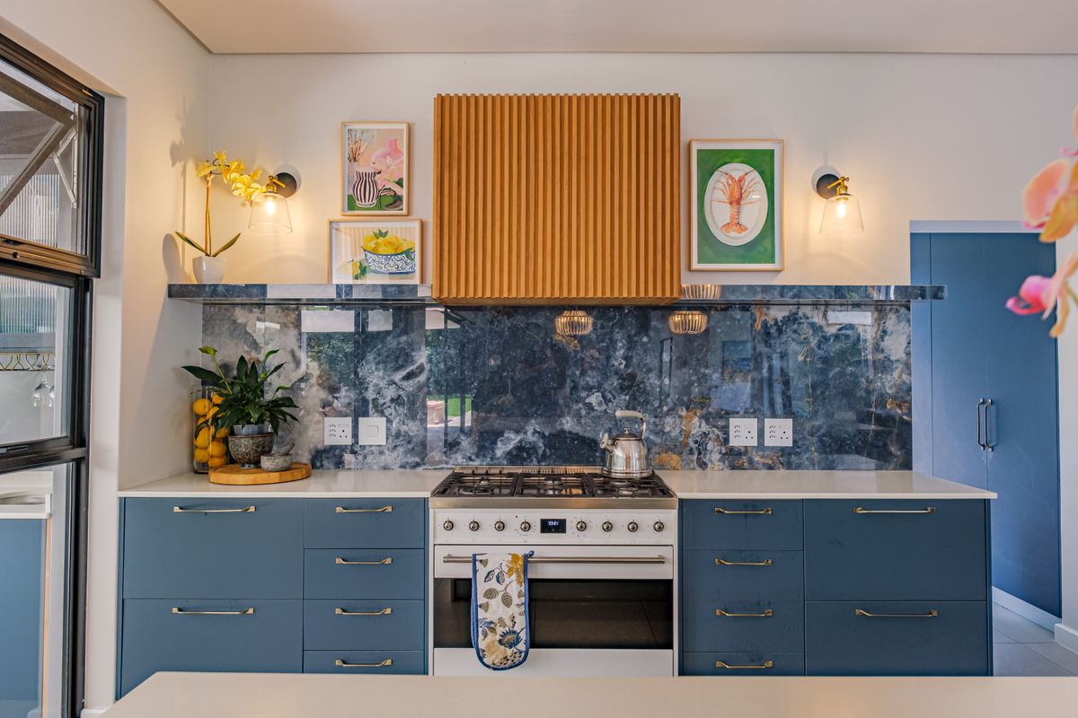 Modern kitchen featuring blue cabinetry, a striking stone splashback, a gas hob with a custom timber extractor hood, and sleek stone countertops.