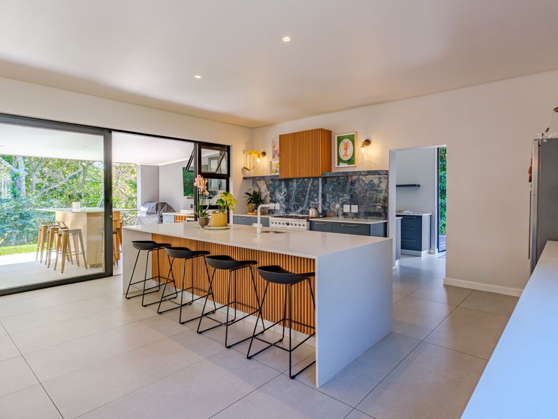 Modern open-plan kitchen featuring a large island with stone countertops, gas cooktop, and seamless flow to the outdoor patio through sliding glass doors.