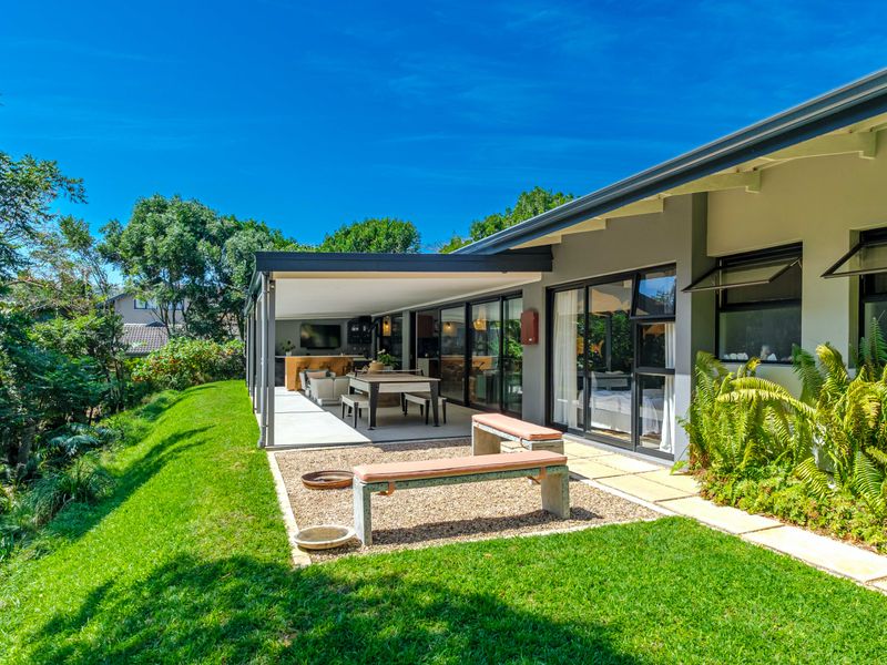 A spacious covered patio area featuring sliding glass doors, concrete flooring, and direct access to a well-maintained landscaped garden.