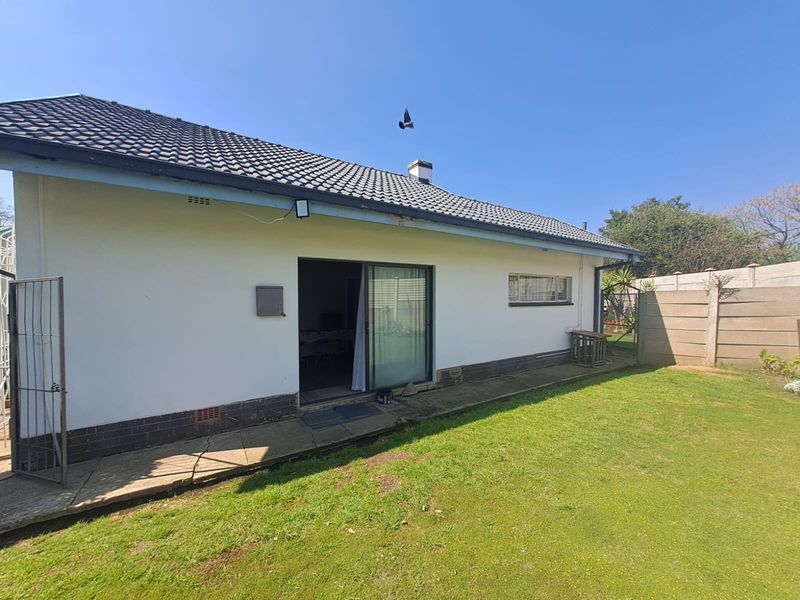 Rear view of the property featuring a tiled roof, sliding door access, concrete pathway, and a private garden area with boundary walling.