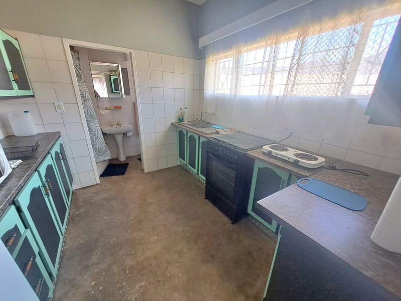 A functional kitchen featuring dated cabinetry, laminate countertops, and a freestanding stove, with an adjacent bathroom visible through the doorway.