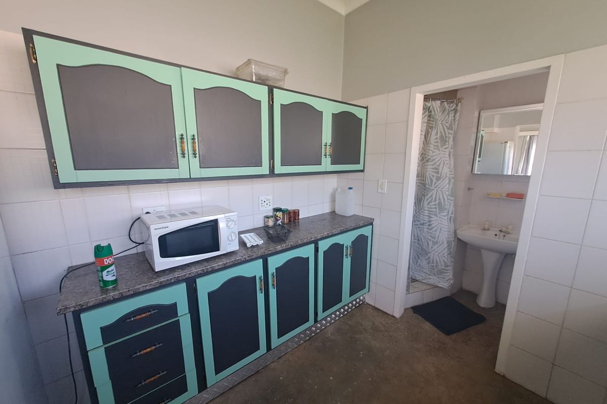 A dated kitchen area featuring built-in cabinetry and a tiled splashback, with an adjacent small bathroom containing a pedestal basin and shower.