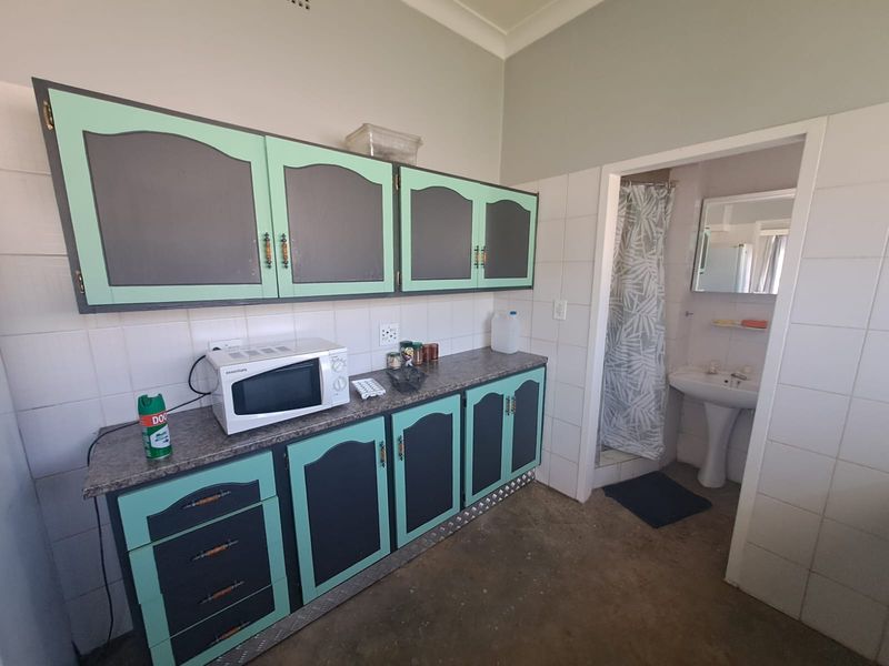 A dated kitchen area featuring built-in cabinetry and a tiled splashback, with an adjacent small bathroom containing a pedestal basin and shower.