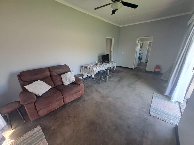 Open-plan living area featuring a ceiling fan and sliding glass door access, with unfinished concrete flooring throughout.
