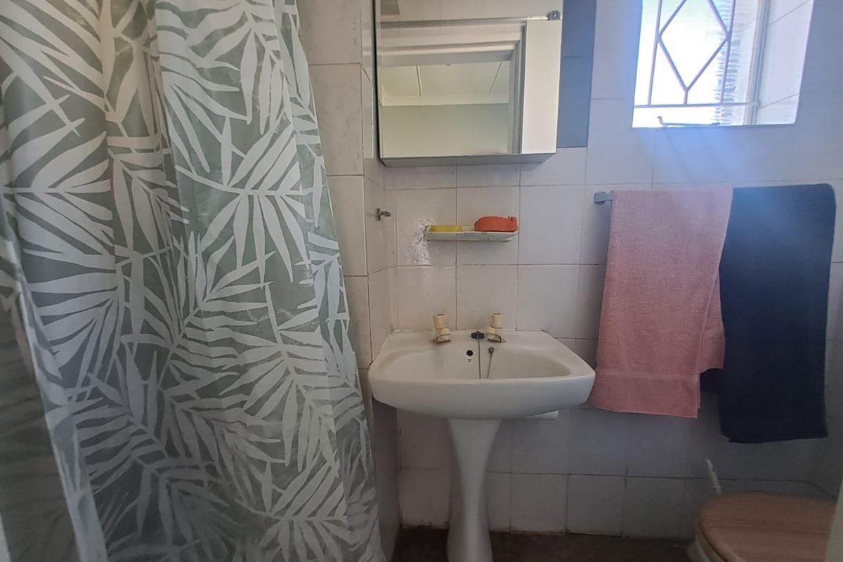 A compact bathroom featuring a pedestal basin, wall-mounted mirror cabinet, and tiled walls with a shower area.