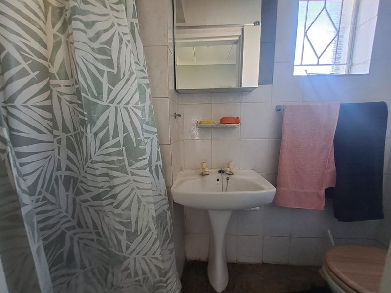 A compact bathroom featuring a pedestal basin, wall-mounted mirror cabinet, and tiled walls with a shower area.