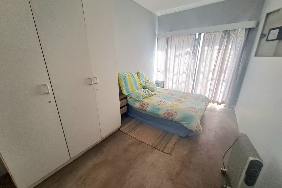 A bedroom featuring built-in cupboards and large windows with curtain rails, providing natural light and functional storage space.
