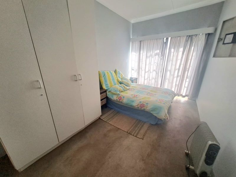 A bedroom featuring built-in cupboards and large windows with curtain rails, providing natural light and functional storage space.
