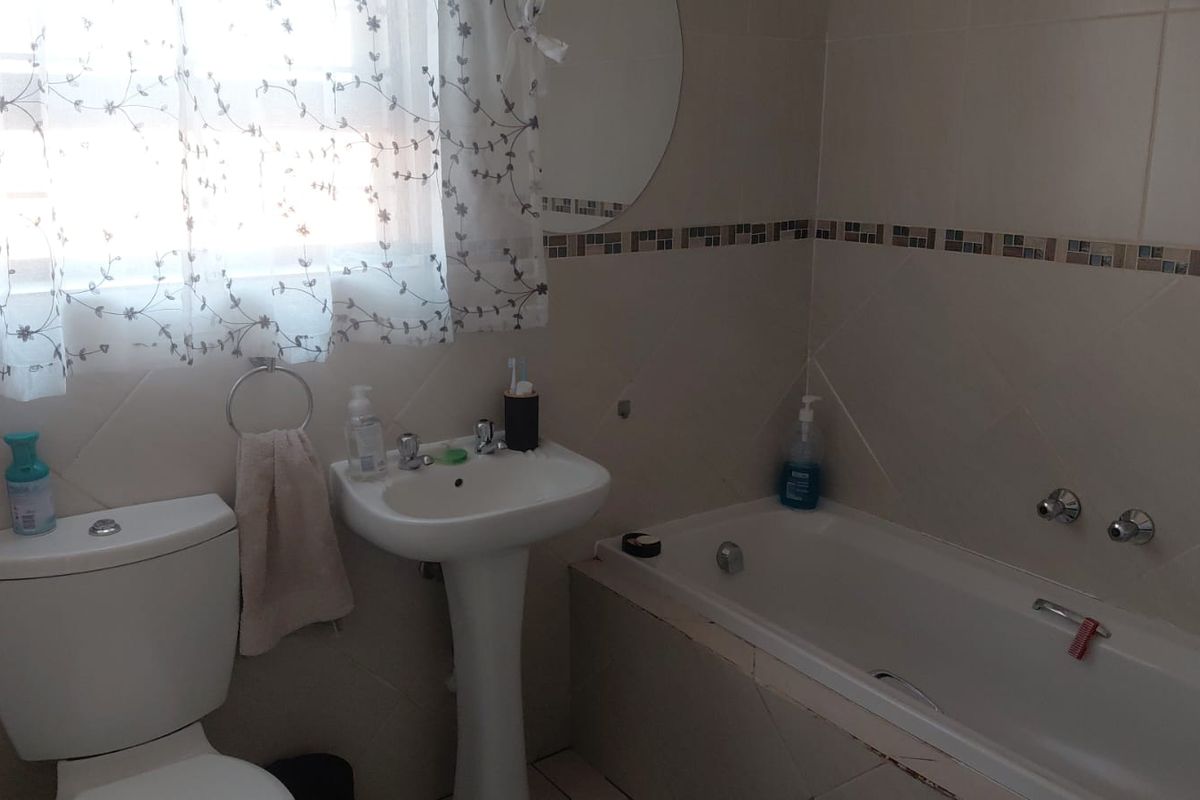 A functional bathroom featuring a pedestal washbasin, built-in bathtub, and neutral wall tiling with a decorative mosaic border.