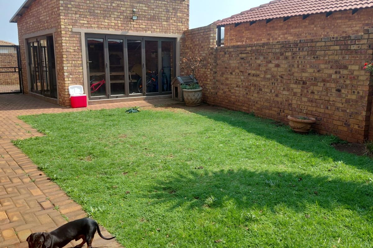 A private rear garden featuring a well-maintained lawn, paved walkway, and face brick boundary walls, with access to the home via folding glass doors.