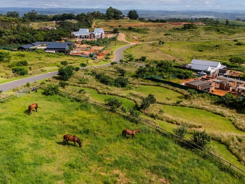 Aerial view of a residential estate featuring open grazing land, post and rail fencing, and surrounding residential construction.