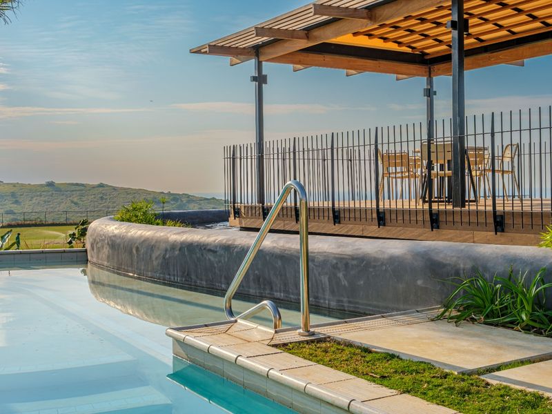 A well-maintained swimming pool area featuring a modern covered patio with timber decking, metal fencing, and scenic landscape views.