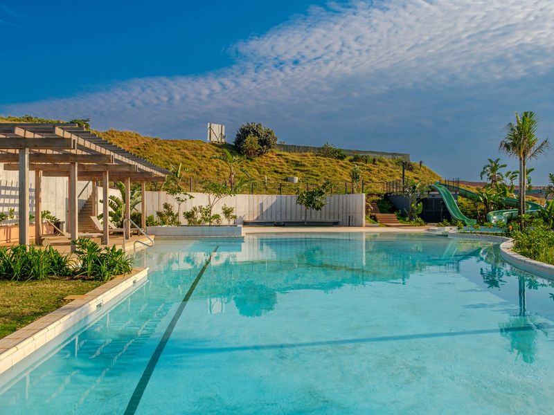 A well-maintained swimming pool area featuring a timber pergola, water slide, and landscaped surroundings set against a hillside backdrop.