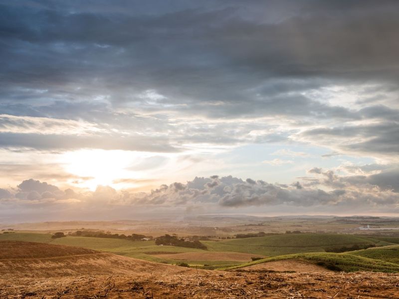 A scenic, expansive view of rolling hills and agricultural landscape under a dramatic sunset sky.
