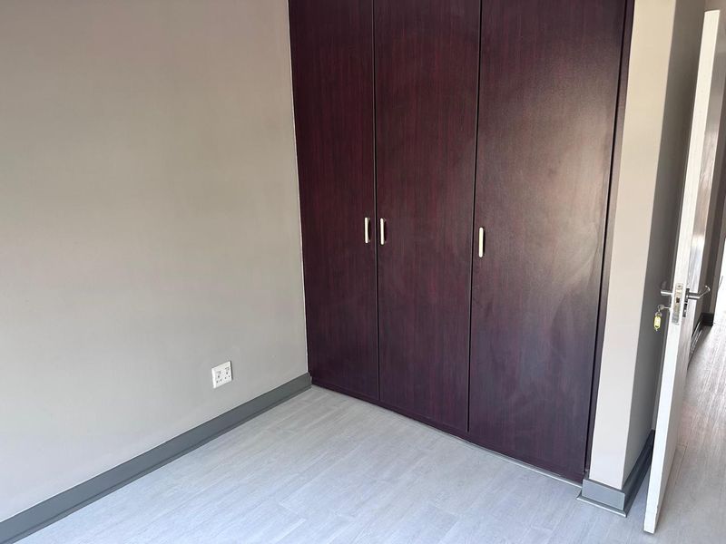A clean, empty bedroom featuring dark wood-finish built-in cupboards, light-toned laminate flooring, and neutral wall paint.