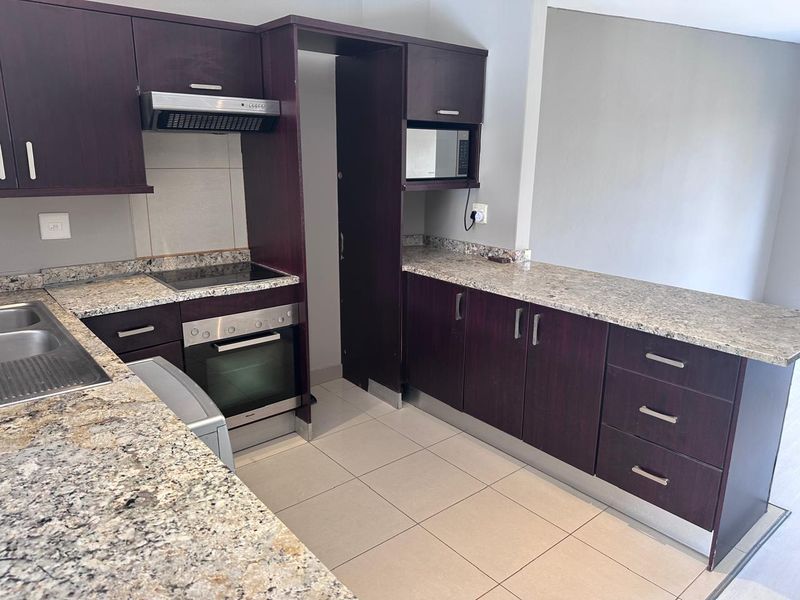 A functional kitchen featuring dark wood cabinetry, granite countertops, built-in oven, hob, extractor fan, and integrated microwave with tiled flooring.