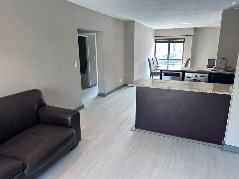 Open-plan living and kitchen area featuring modern granite countertops, built-in cabinetry, integrated appliances, and light-toned laminate flooring throughout.