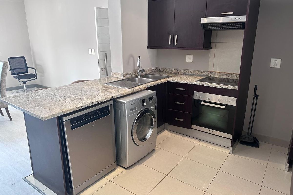 Compact kitchen featuring dark wood cabinetry, granite countertops, built-in oven, electric hob, and integrated space for laundry and dishwashing appliances.