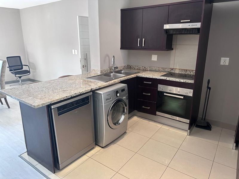 Compact kitchen featuring dark wood cabinetry, granite countertops, built-in oven, electric hob, and integrated space for laundry and dishwashing appliances.