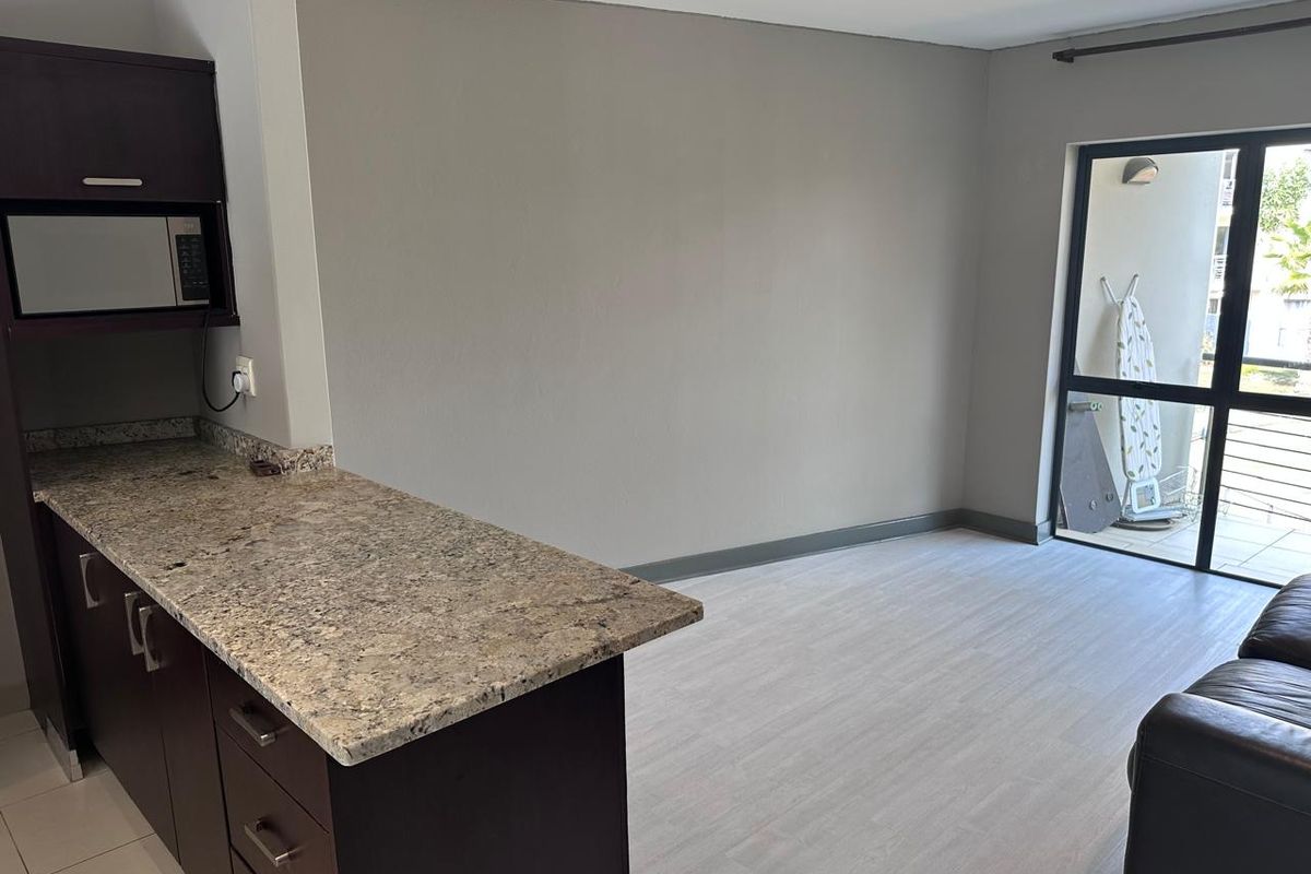 Open plan living area featuring a kitchen with granite countertops, built-in cabinetry, and a sliding glass door leading to an outdoor balcony.