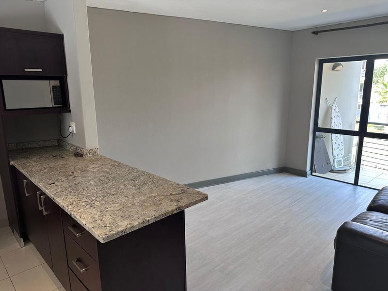 Open plan living area featuring a kitchen with granite countertops, built-in cabinetry, and a sliding glass door leading to an outdoor balcony.