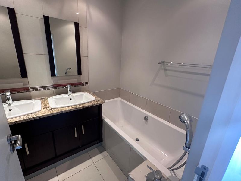 A clean, modern bathroom featuring a double vanity with granite countertops, a built-in bathtub, and neutral wall tiling.