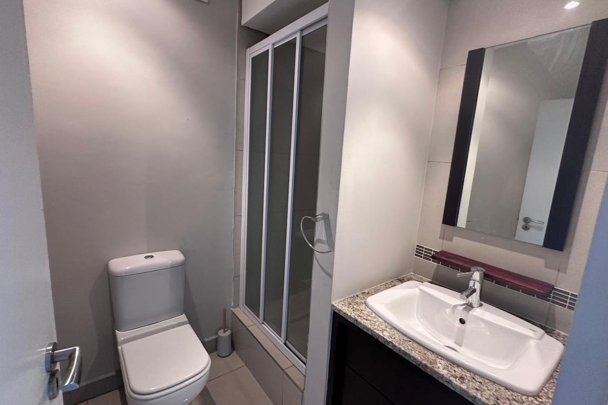 A clean, modern bathroom featuring a shower enclosure, vanity with granite countertop, basin, and wall-mounted mirror.