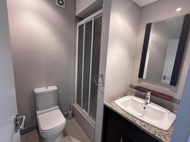 A clean, modern bathroom featuring a shower enclosure, vanity with granite countertop, basin, and wall-mounted mirror.