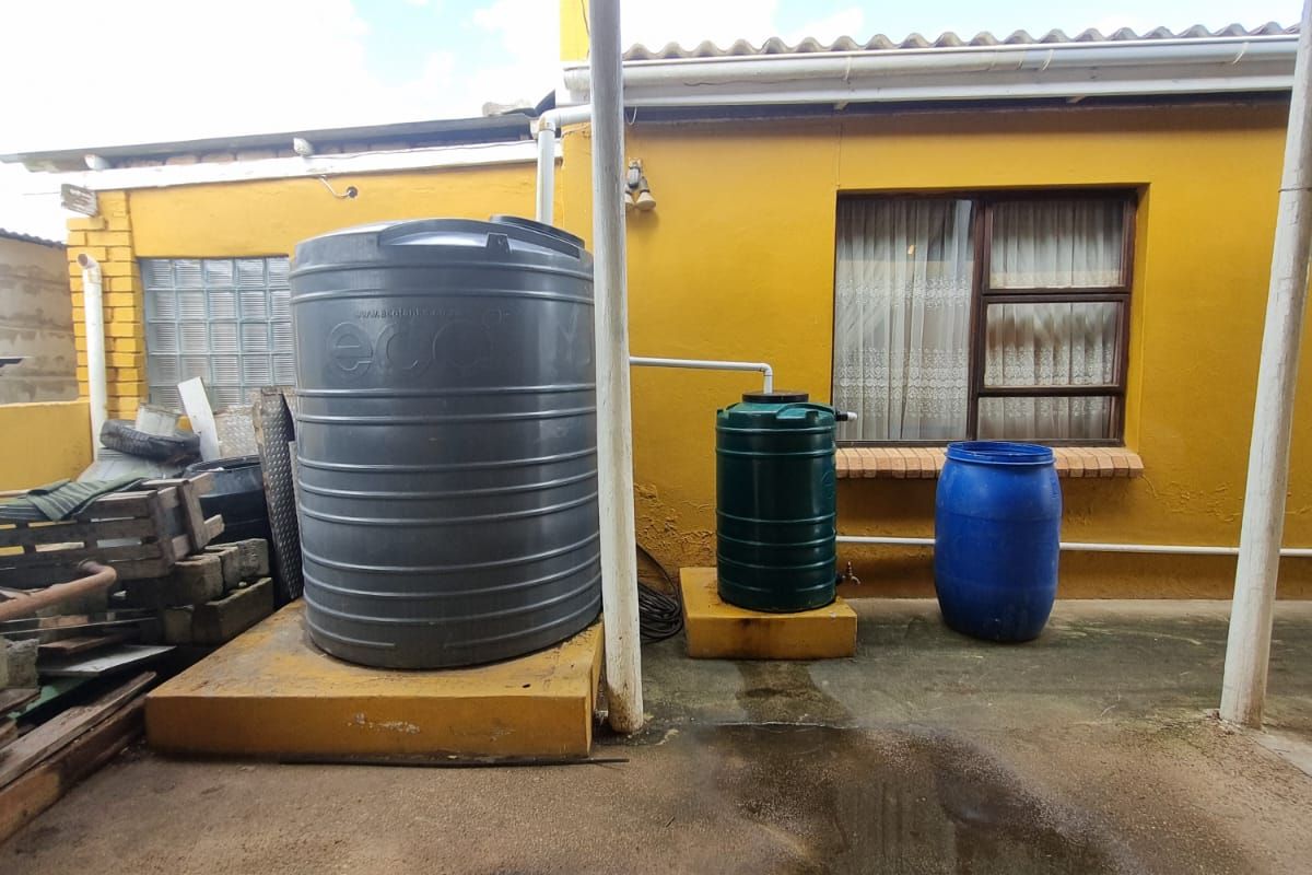 Rear exterior area featuring a covered patio with multiple water storage tanks, concrete flooring, and a yellow painted facade.