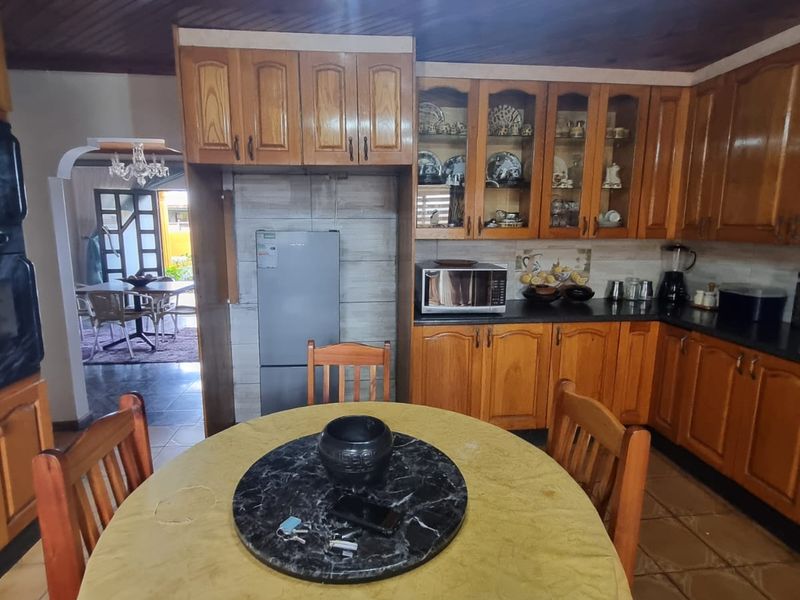 A traditional kitchen featuring extensive wooden cabinetry, timber-clad ceilings, and tiled flooring, with an open-plan layout leading to an adjacent dining area.