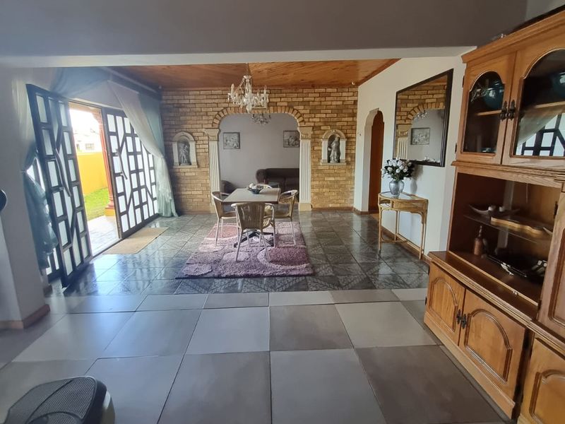 Spacious open-plan living and dining area featuring an exposed timber ceiling, brick feature wall, and direct access to the outdoor patio.