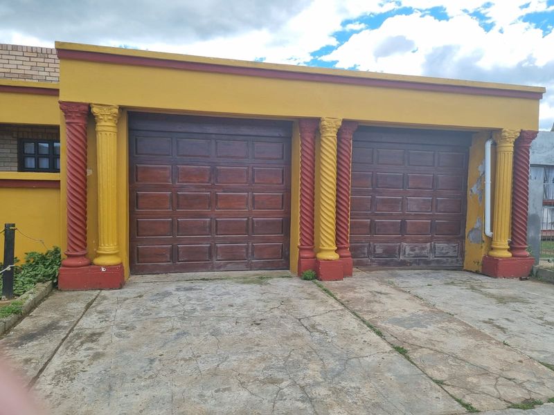 A double garage featuring wooden sectional doors and decorative columns, set against a yellow exterior facade with a concrete driveway.