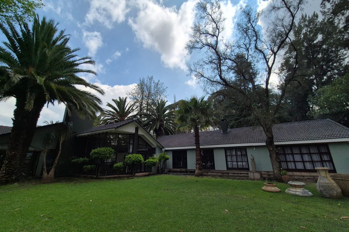 A spacious rear garden featuring a well-maintained lawn, mature palm trees, and a view of the home's rear elevation with tiled roofing.