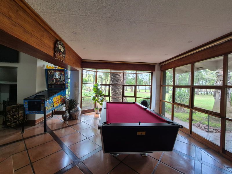 Spacious living area featuring large timber-framed windows with garden views, terracotta tiled flooring, and exposed timber ceiling beams.