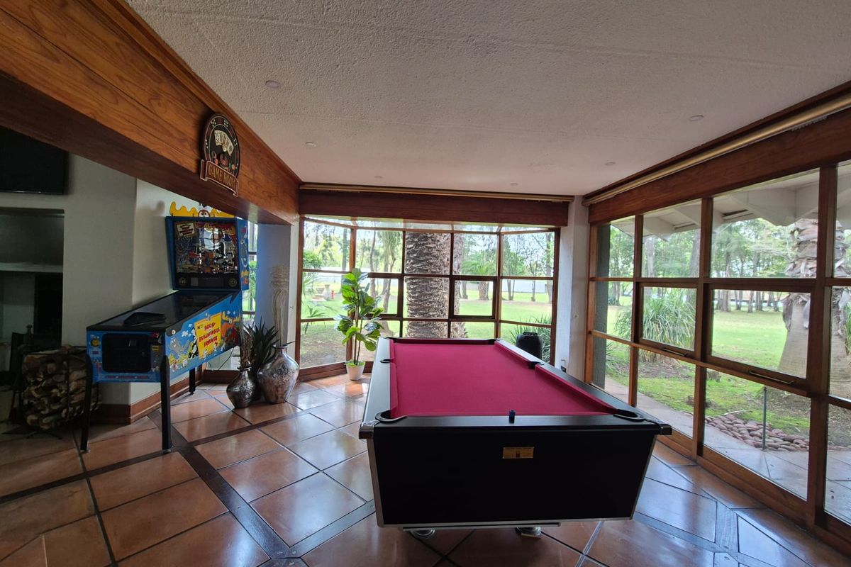 Spacious living area featuring large timber-framed windows with garden views, terracotta tiled flooring, and exposed timber ceiling beams.