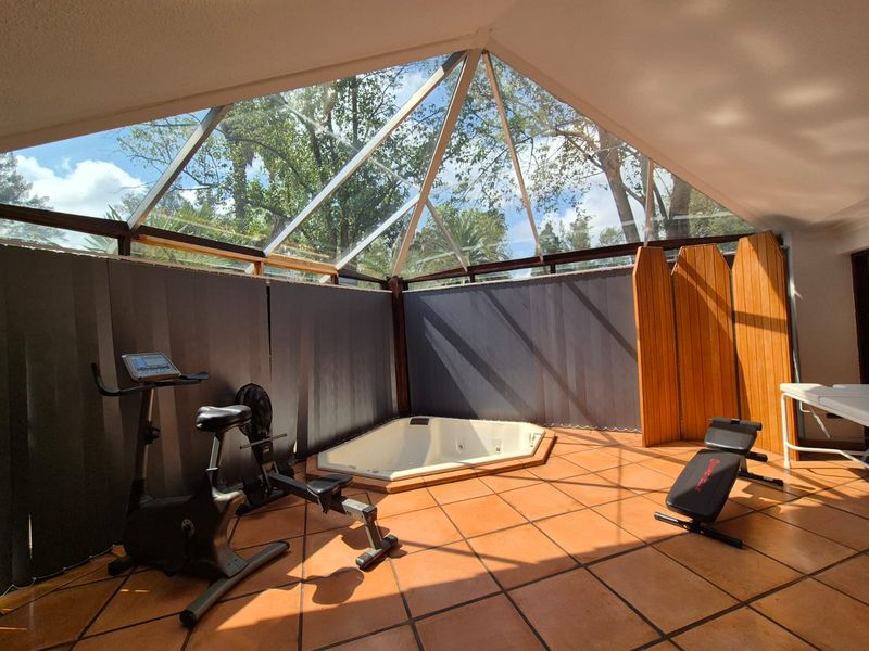 A bright gym area featuring a pitched glass roof, terracotta tiled flooring, and a built-in corner spa bath.