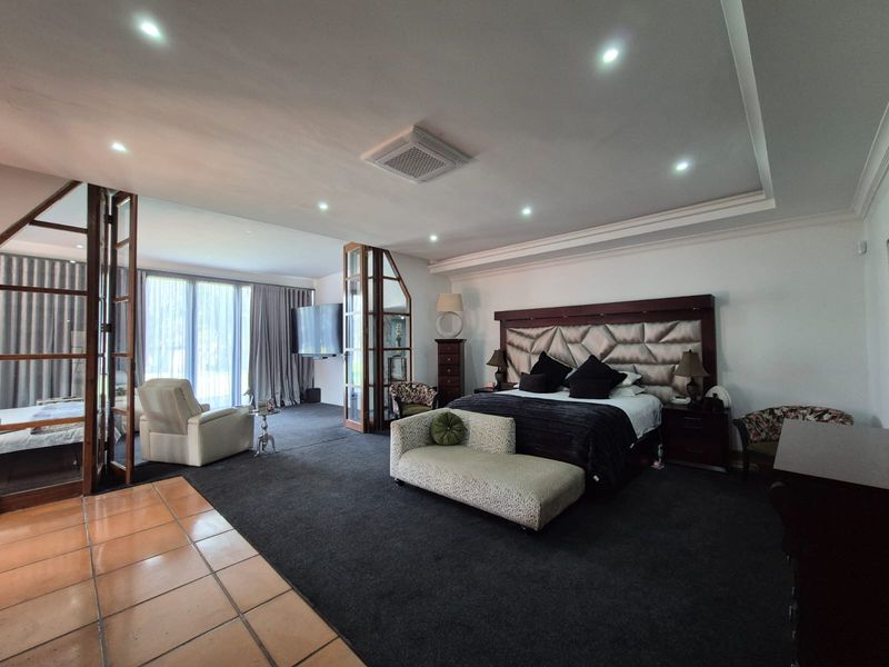 Spacious primary bedroom featuring a tray ceiling with recessed lighting, ducted air conditioning, and a glass-partitioned seating area with direct outdoor access.