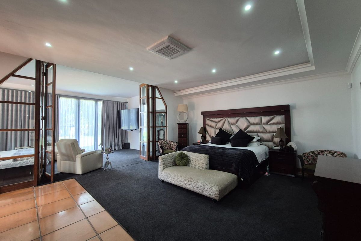Spacious primary bedroom featuring a tray ceiling with recessed lighting, ducted air conditioning, and a glass-partitioned seating area with direct outdoor access.