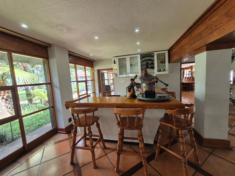 A dedicated bar area featuring a built-in timber counter, glass-fronted cabinetry, wine storage, and large windows overlooking the garden.