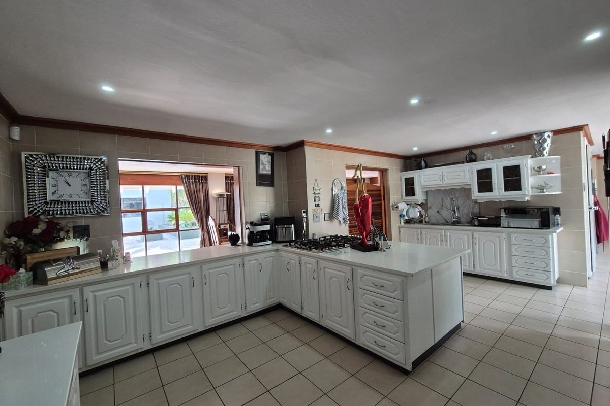 Spacious kitchen featuring white cabinetry, a central island with a gas cooktop, tiled flooring, and ample counter space with integrated sink.