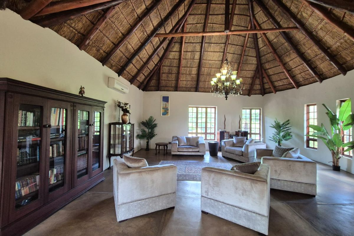 Spacious living room featuring a high vaulted thatched ceiling with exposed timber rafters, polished concrete floors, and large timber-framed windows.