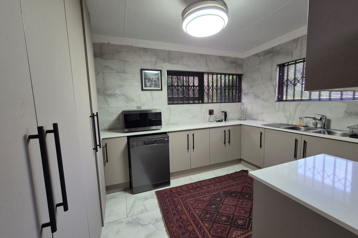 Modern kitchen featuring sleek built-in cabinetry, stone countertops, tiled backsplash, and high-quality finishes with security bars on the windows.